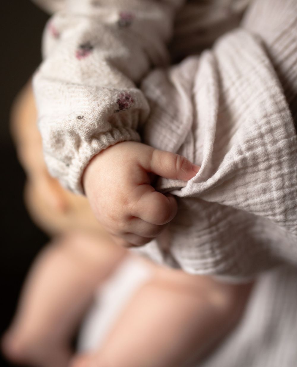 Close-up shots of tiny baby hands gently grasping soft white fabric in serene lighting.