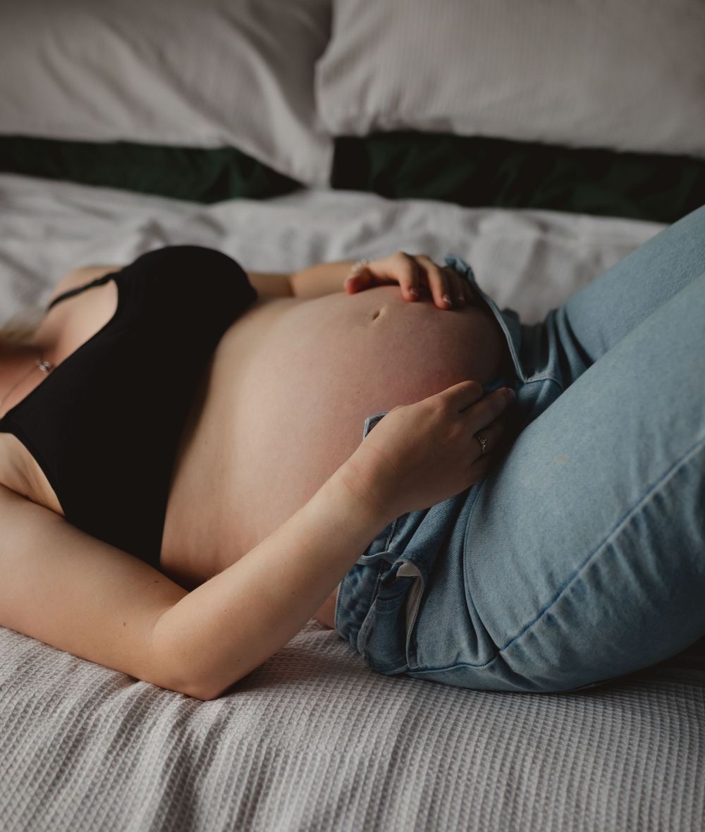 Gentle moody portrait of pregnant belly on bed with soft bedding and natural light.