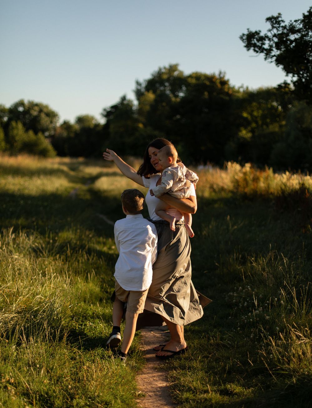 Family playing and dancing together on a nature trail during golden hour.