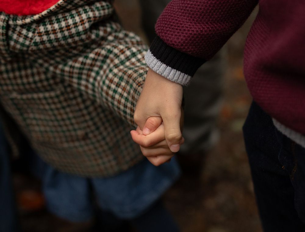 Two people holding hands in close up shot showing checked jacket and burgundy sweater sleeves.