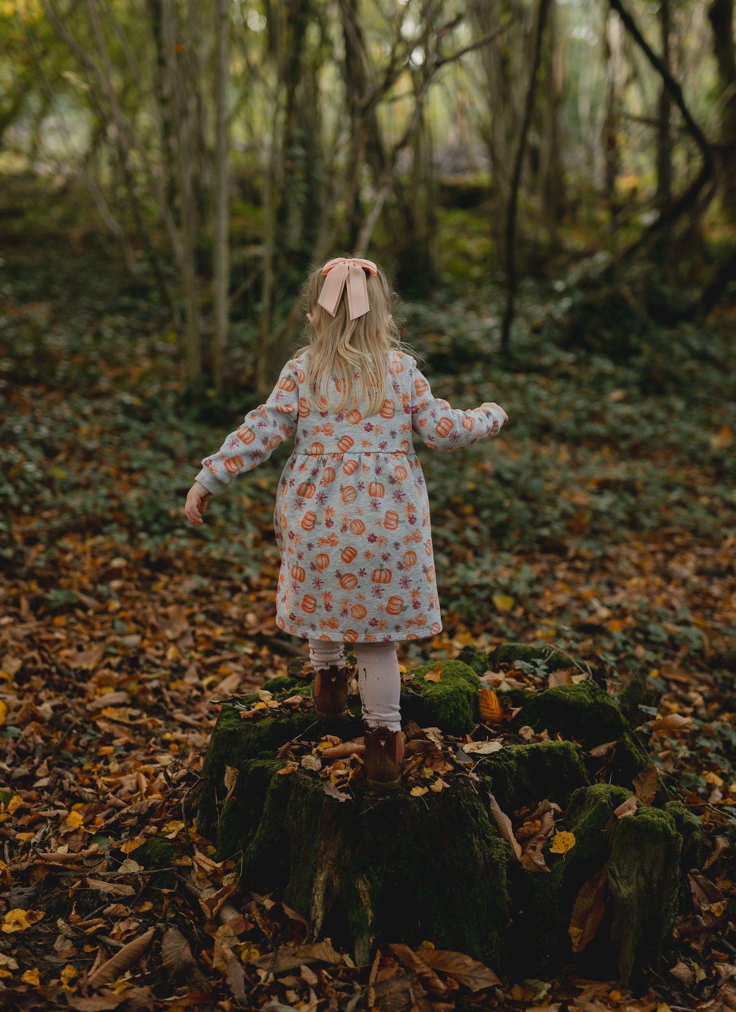 A series of photos showing someone walking through autumn leaves in a floral dress and white tights in a wooded setting.