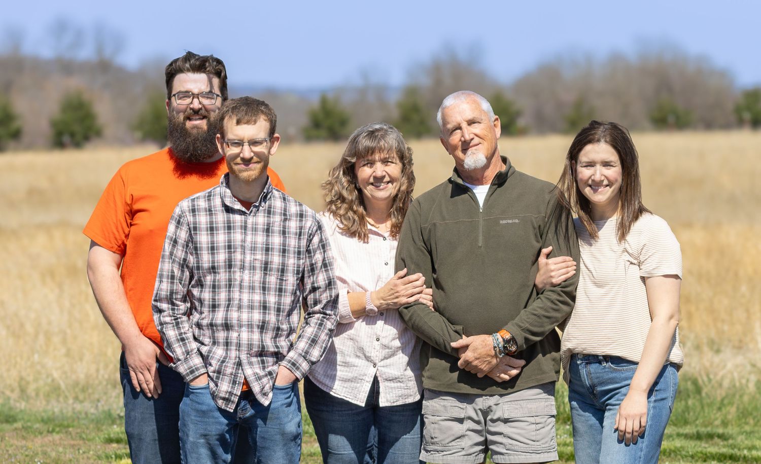 Extended family gathering outdoors in a sunny field for a casual group photo.