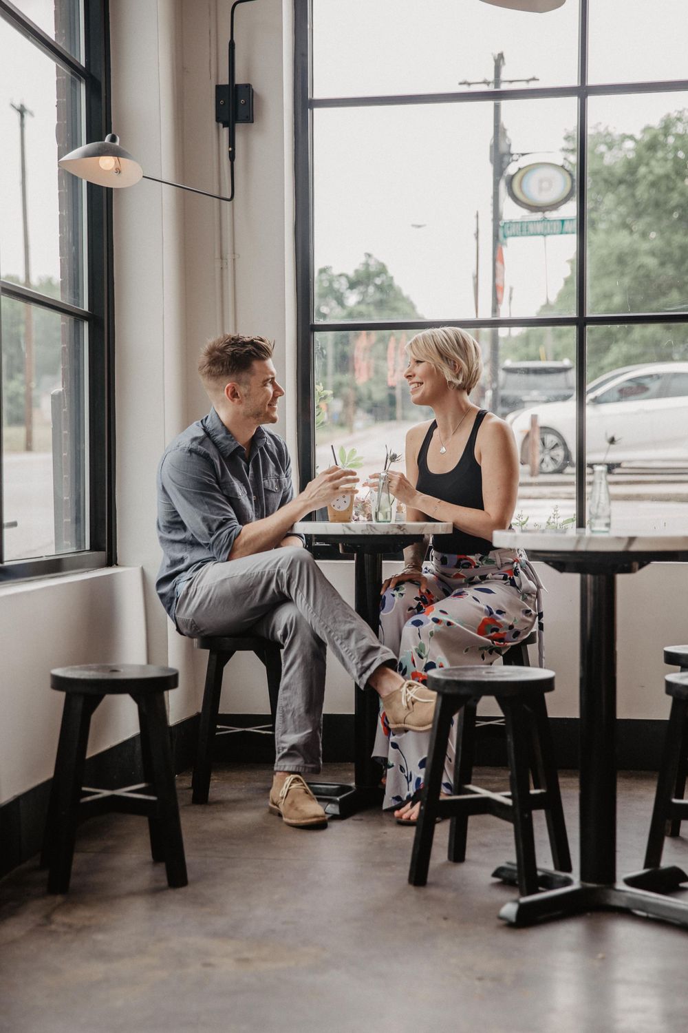 A couple enjoying drinks together at a cafe table by large windows.