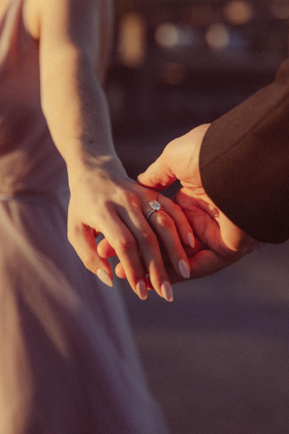 Close-up of hands with an engagement ring touching in warm sunset lighting.