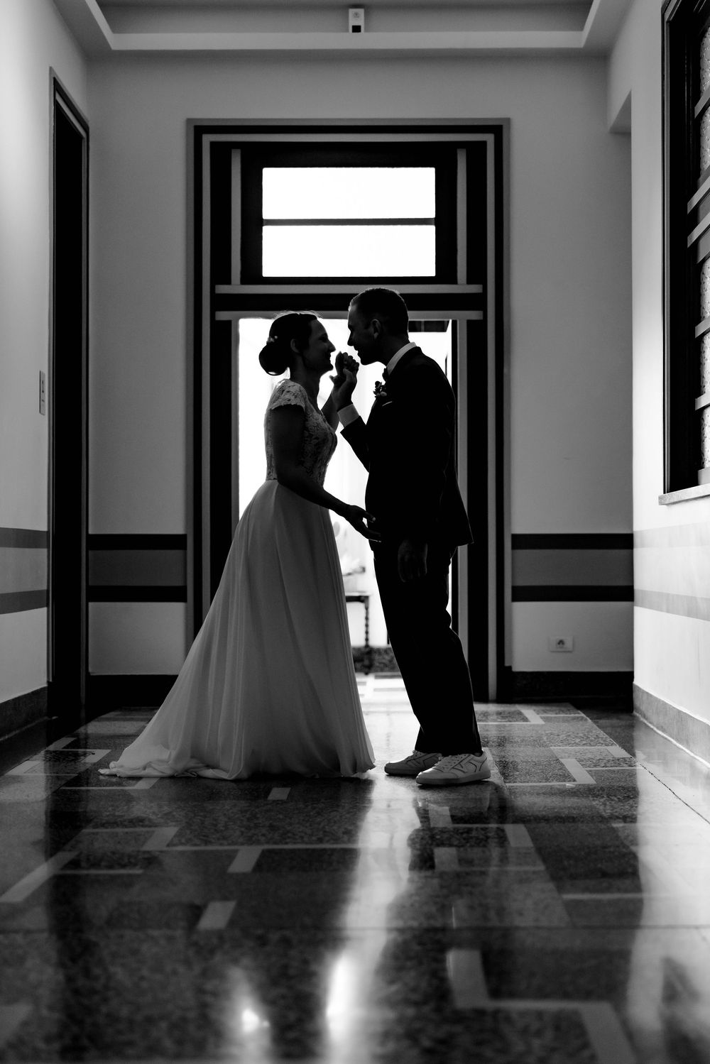 Black and white silhouette of a bride and groom sharing a romantic moment in an elegant hallway.