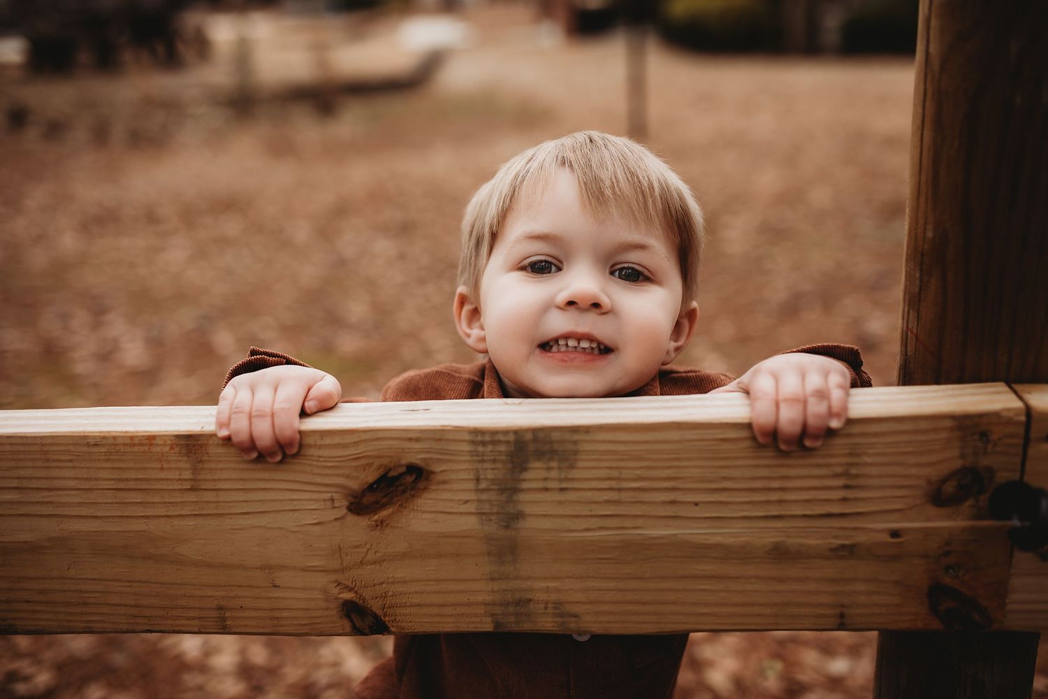 Child peeks playfully over wooden fence railing.
