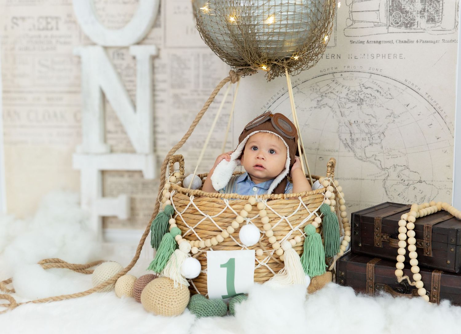 Baby in hot air balloon basket prop with gold balloon and vintage travel decor.