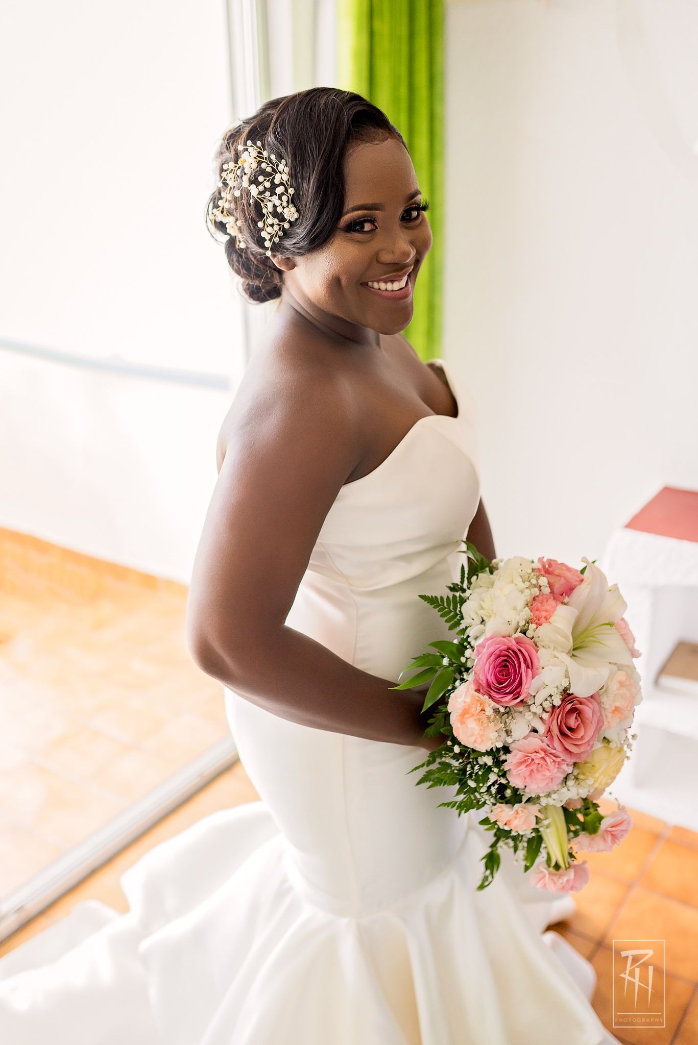 Elegant bride in white strapless gown holds pink and white bouquet while smiling over shoulder.