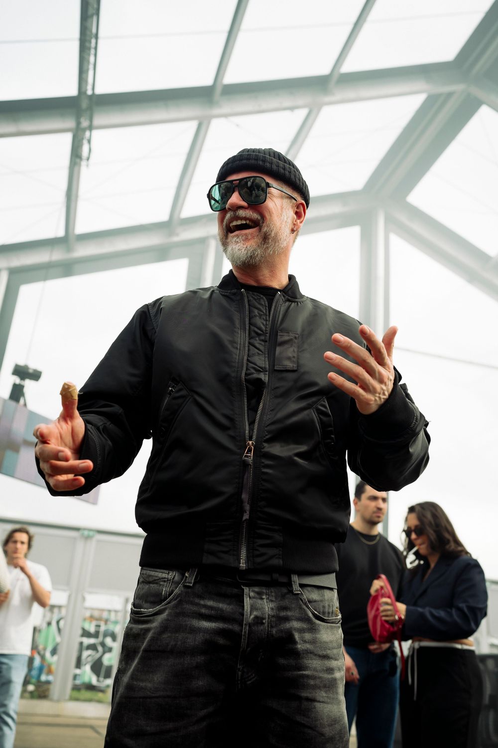 Person in black outfit and sunglasses dancing expressively in a glass-roofed venue.