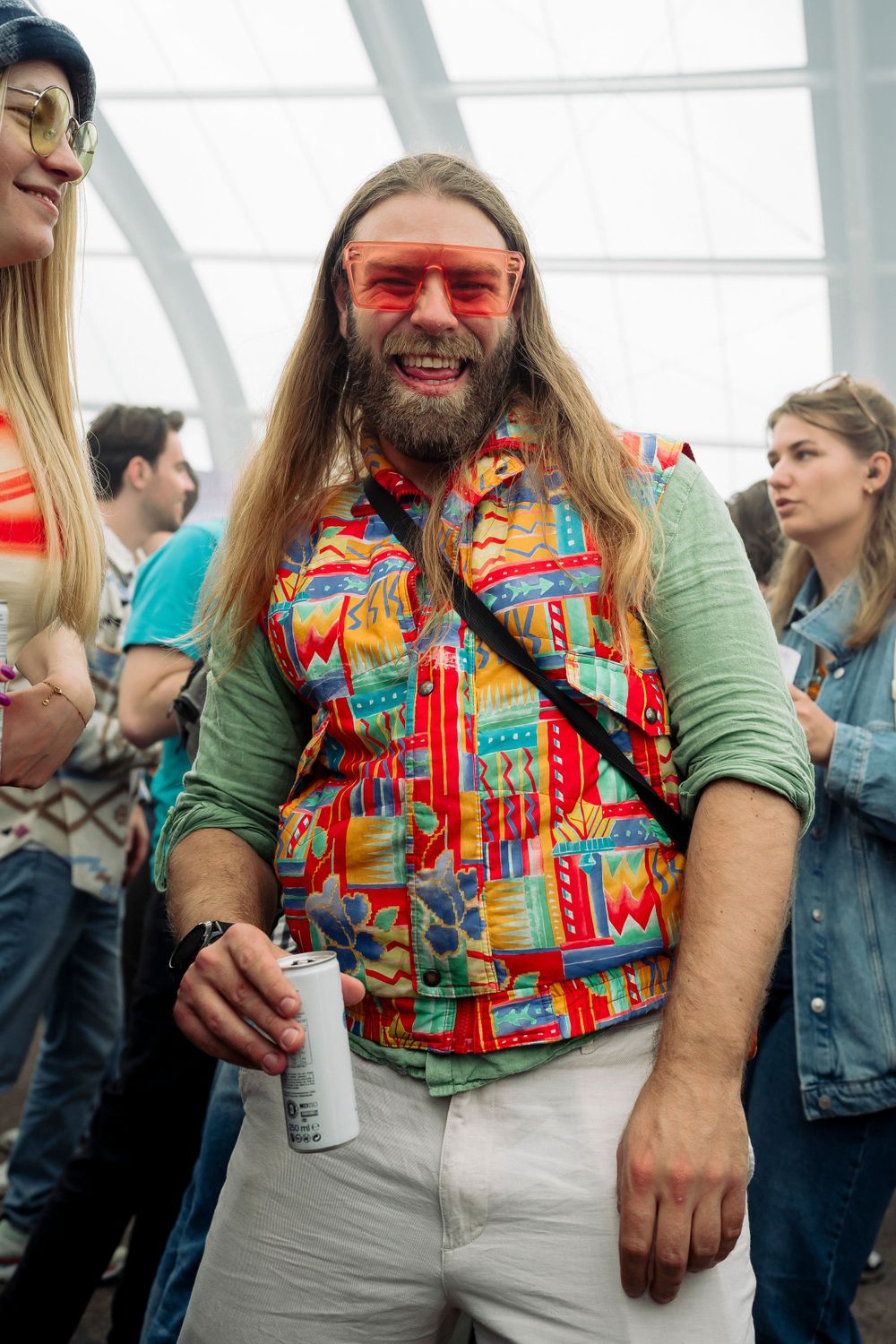 Person in colorful patterned shirt and green sleeves enjoying a drink at an indoor party.