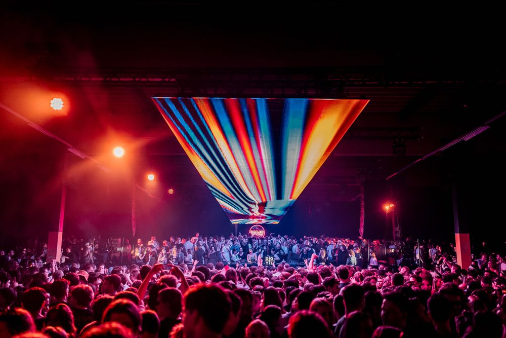 Colorful light show illuminates silhouetted crowd at nighttime event.