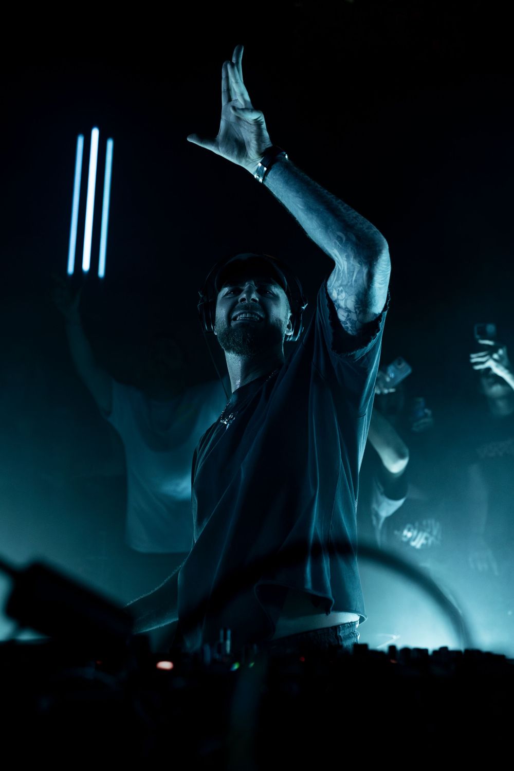 DJ performing on stage with dramatic blue lighting and raised arm during an energetic nightclub performance.