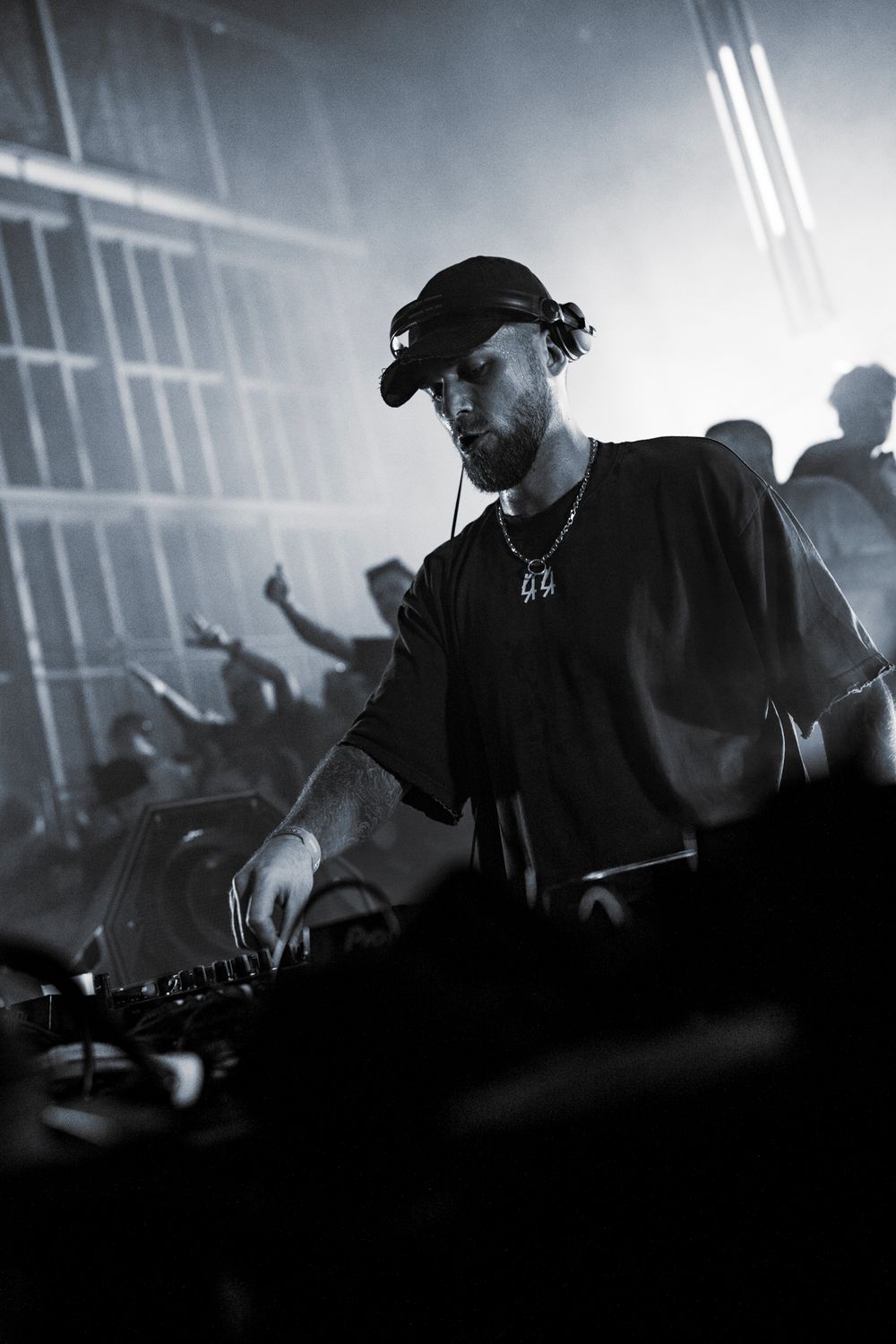 Silhouetted DJ performing at decks with backlit crowd and atmospheric smoke effects.