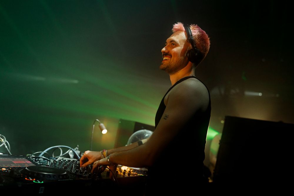 Dark nightclub venue with silhouetted DJ equipment and atmospheric green lighting.