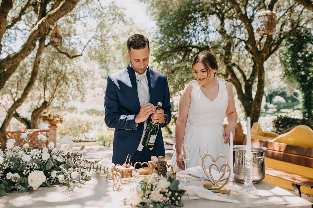 Couple pouring champagne at outdoor wedding reception table.