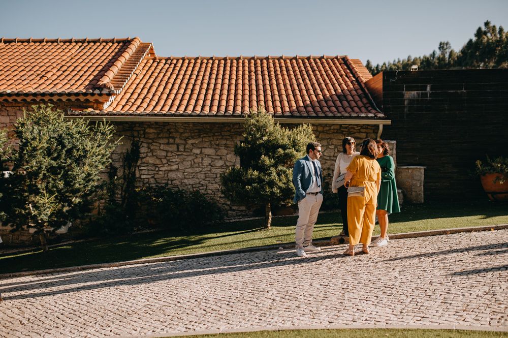 Guests wearing formal attire stand near a rustic stone building with terracotta roof tiles.