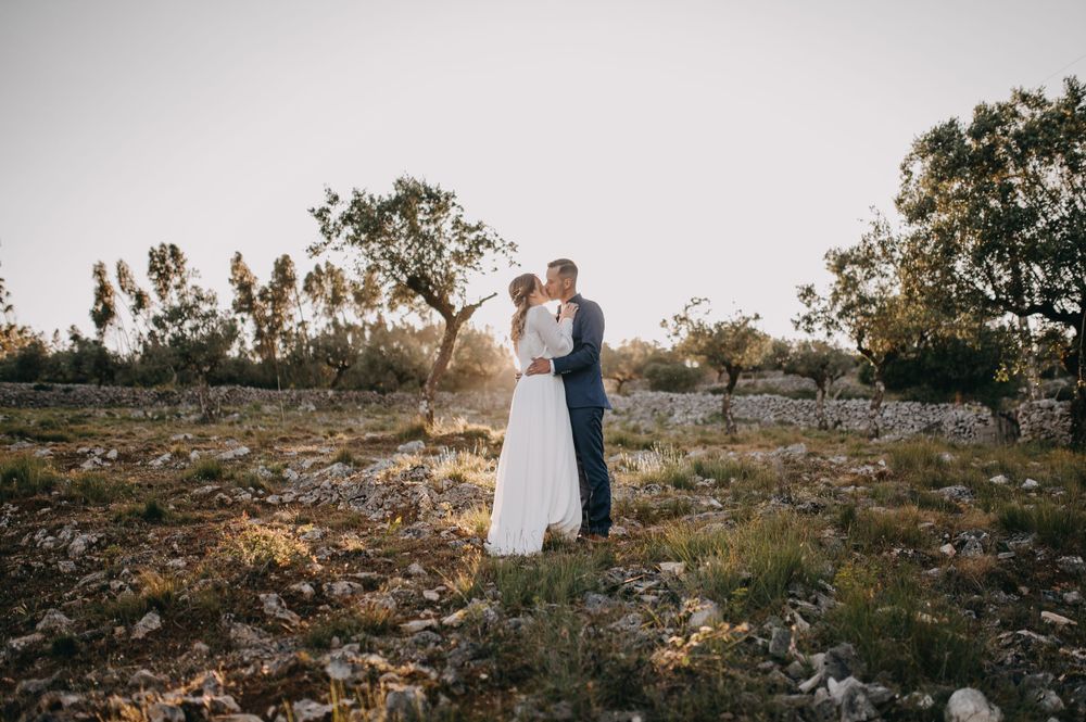 A romantic sunset wedding photo of a couple on a rocky hillside with trees in the background.