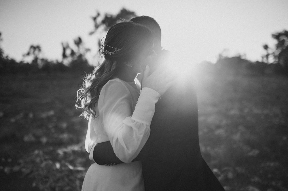 A dramatic black and white silhouette of newlyweds backlit by golden sunlight.