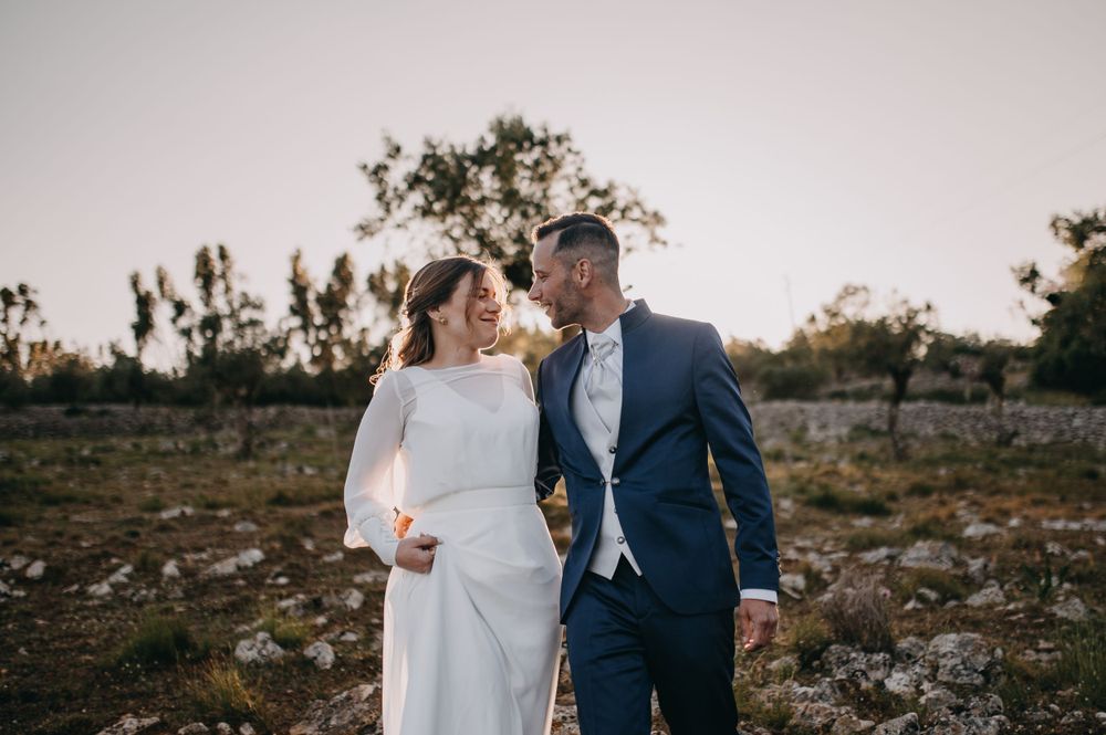 A couple in wedding attire walking together on a rugged outdoor terrain at golden hour.
