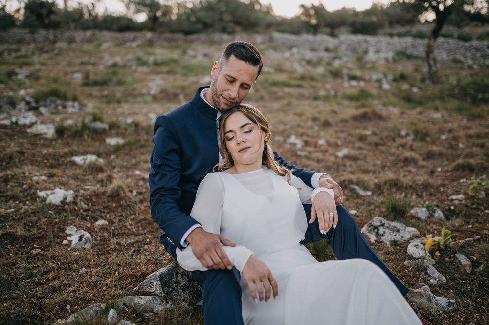 An intimate wedding portrait of a couple relaxing on rocky ground at sunset.