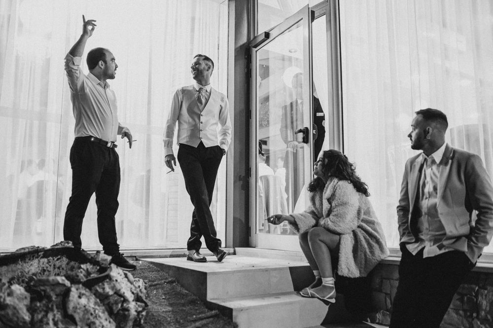 A group of friends laughing and posing casually in front of white curtained windows in black and white.