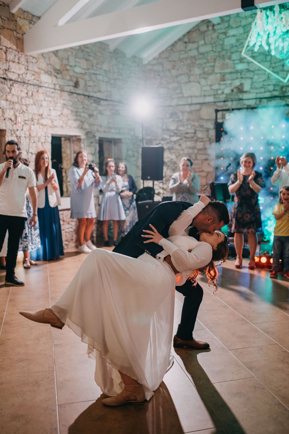 A dramatic wedding dip dance move captured under blue lighting in a rustic venue.