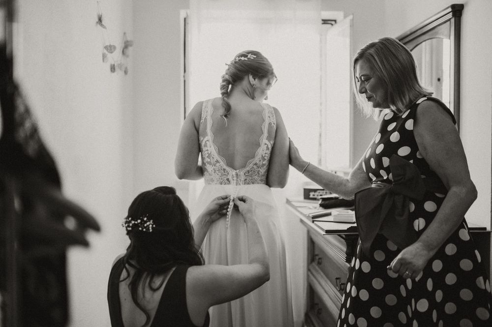 Black and white photo of bridal preparations with dress adjustments being made.
