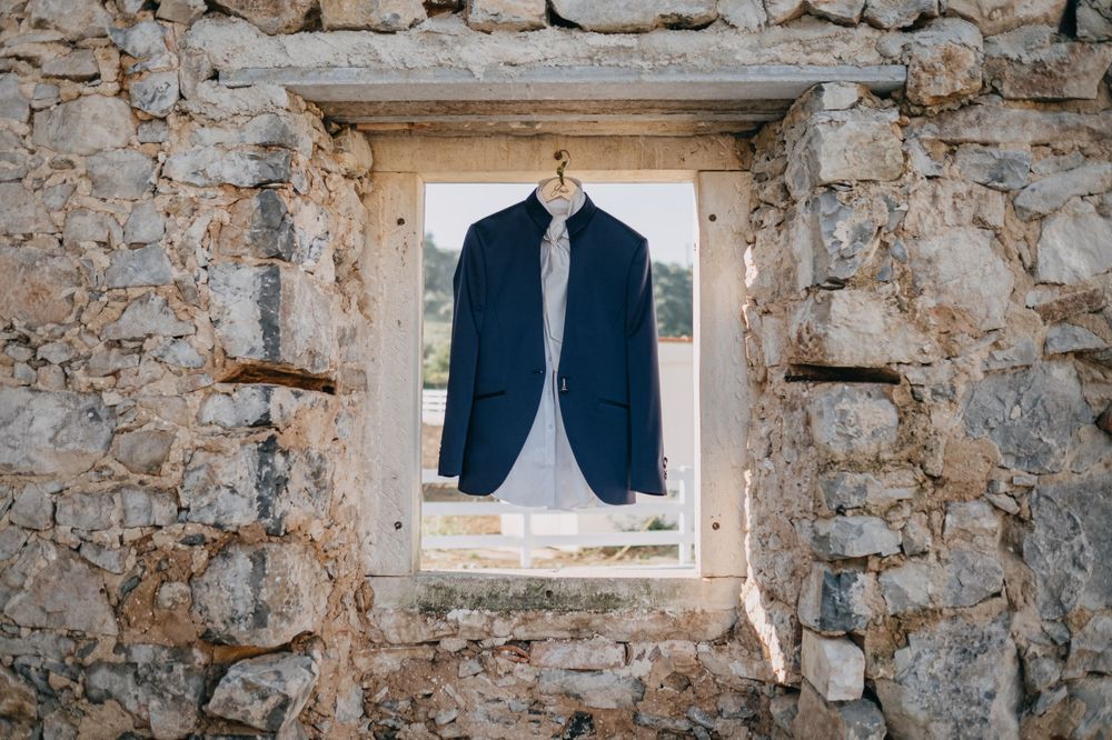A navy blue suit jacket hangs in a stone window frame of an old rustic wall.