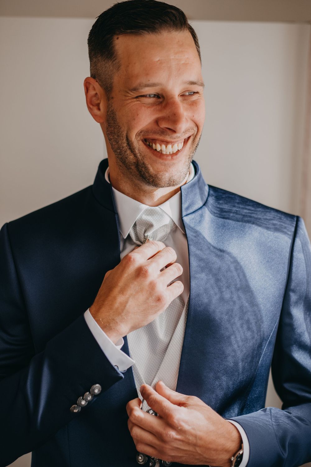 Well-dressed person adjusting a light-colored tie against a navy suit.