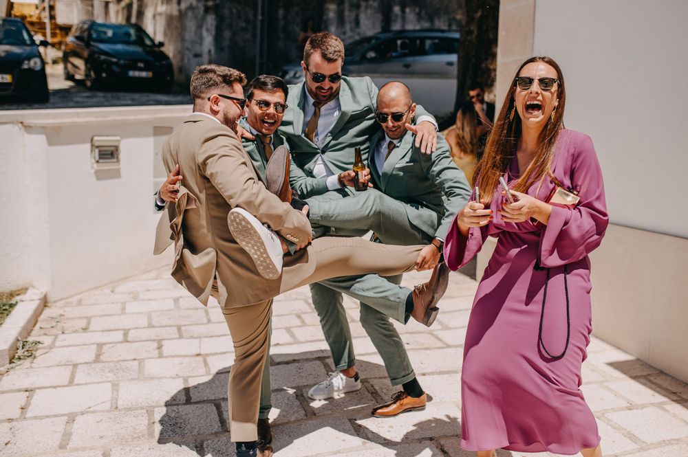 Wedding guests playfully posing and jumping outside, with one person wearing a pink suit.