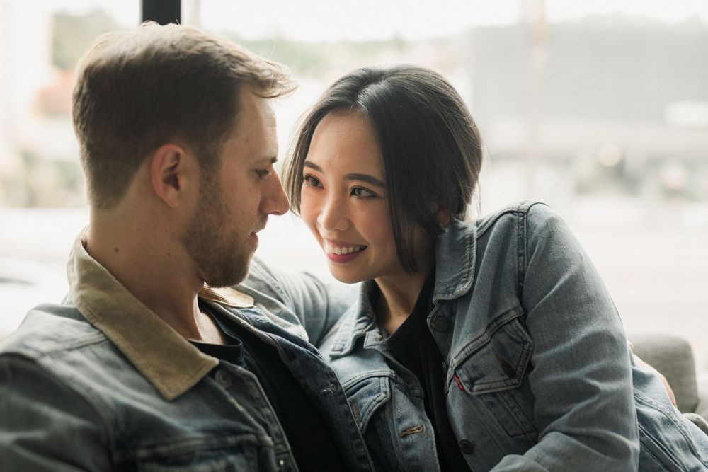 Intimate couple moment by window with soft natural lighting and casual denim attire.