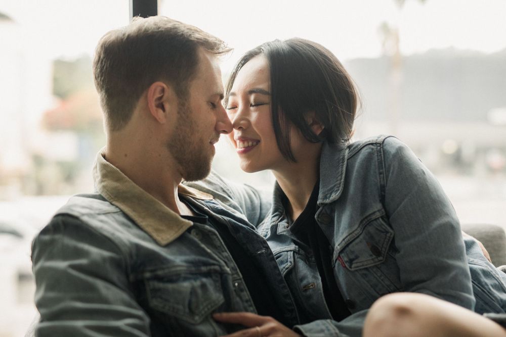 Tender moment between couple lounging by window in matching denim jackets.