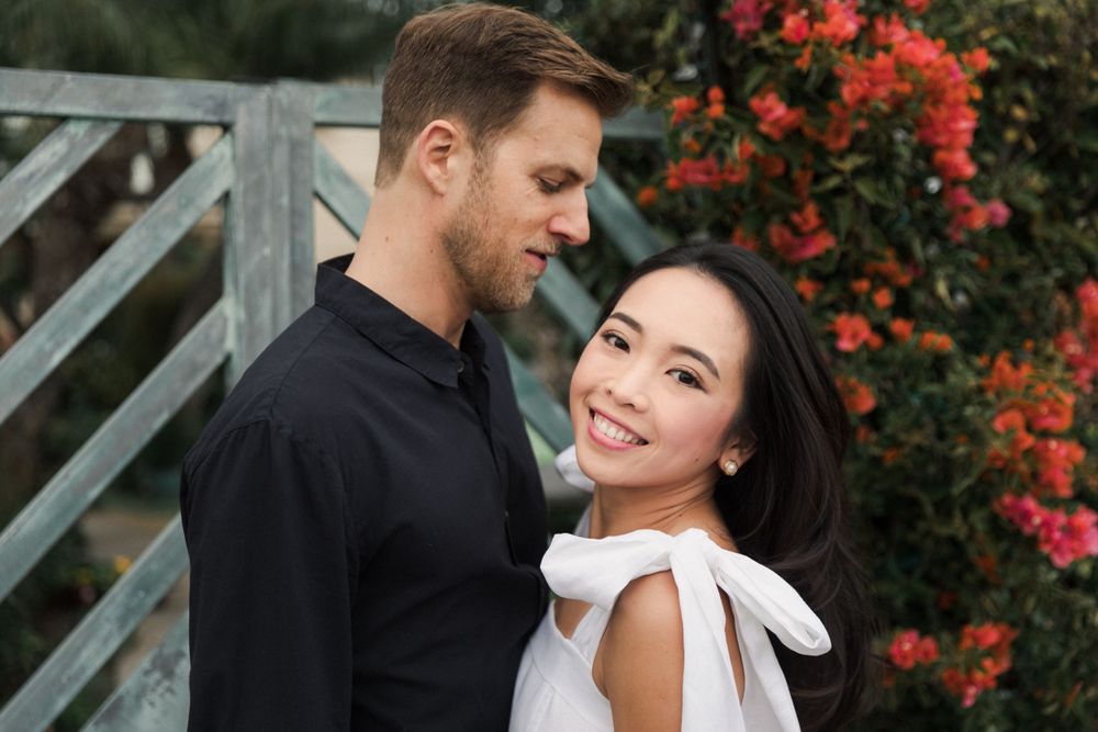 Romantic portrait of couple against garden backdrop with red flowers, wearing coordinated black and white outfits.