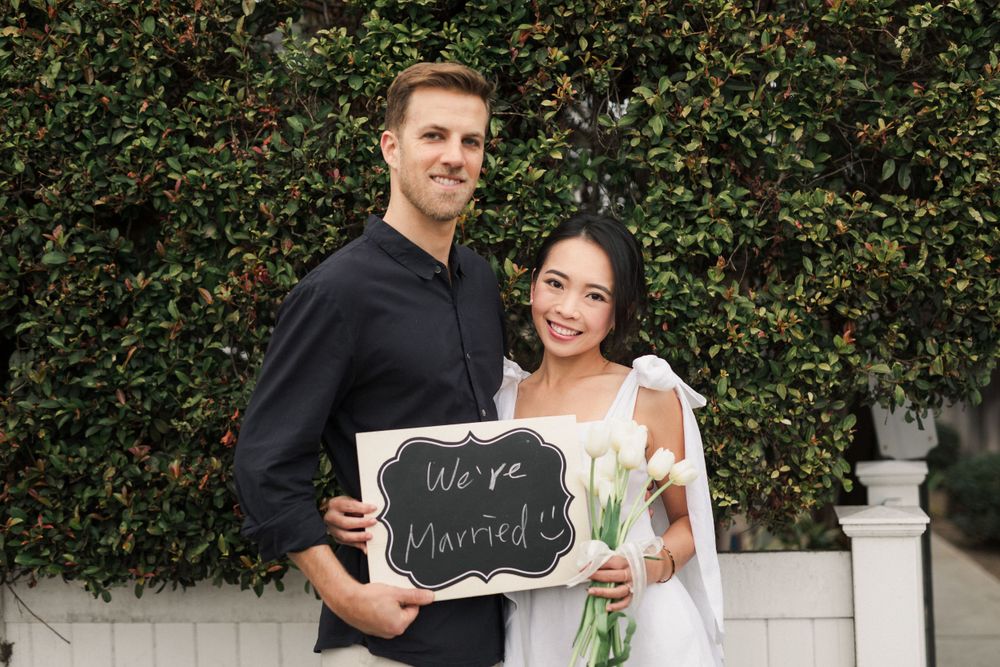 A couple poses with a chalkboard sign against a green hedge backdrop.