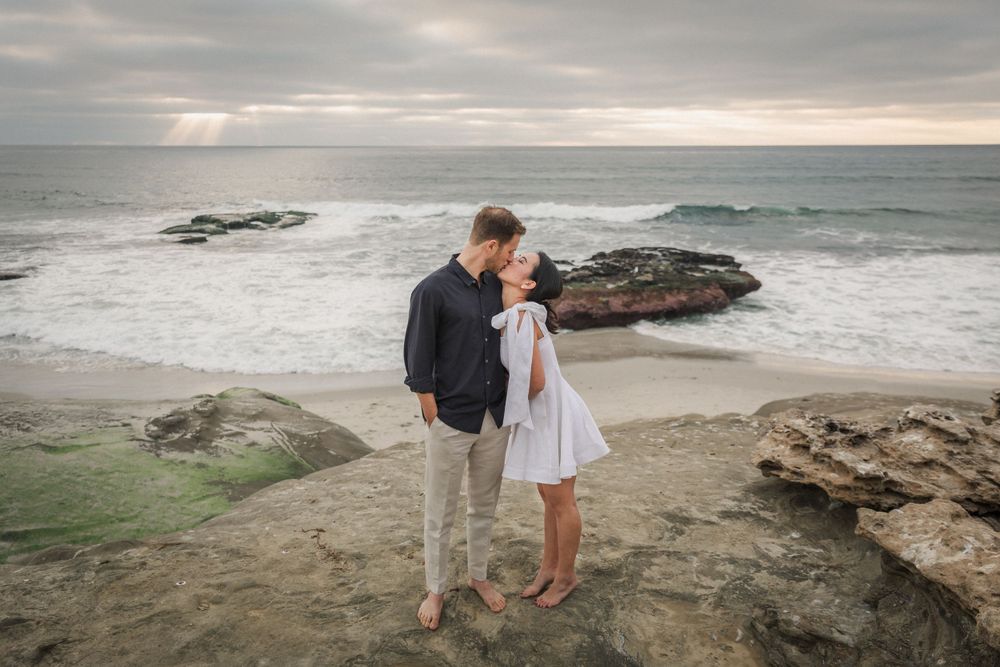 A couple shares an intimate moment on rocky coastal cliffs during sunset.