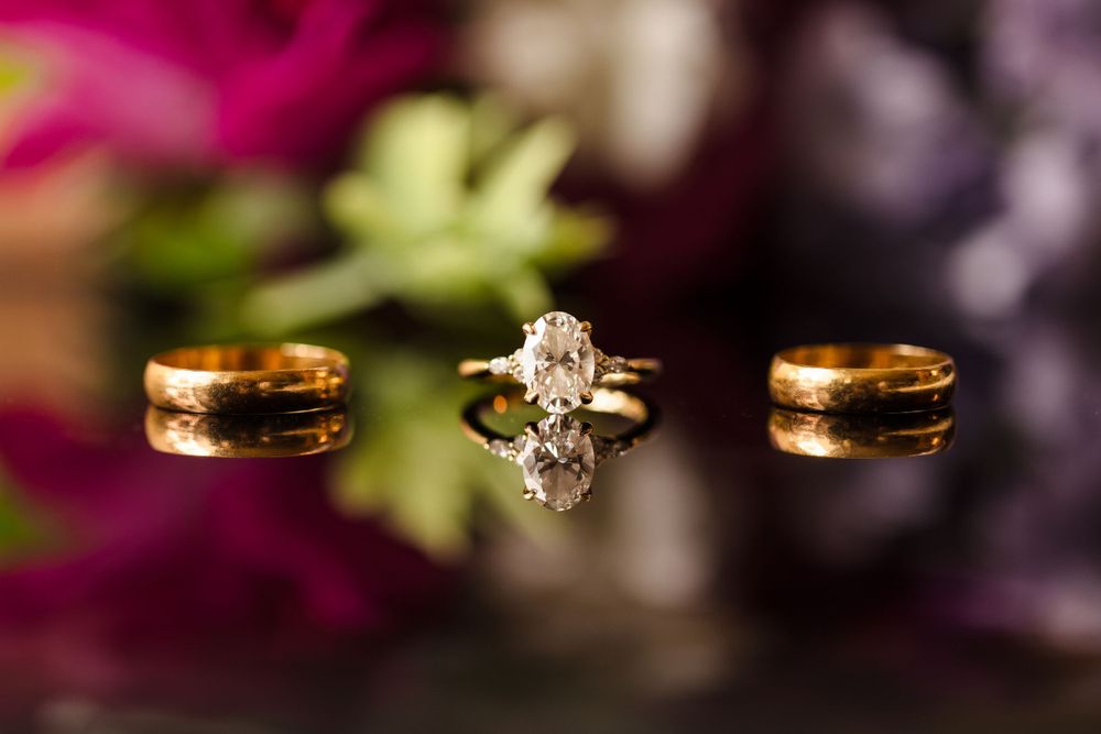 Three wedding rings including a diamond engagement ring displayed against a blurred floral background.