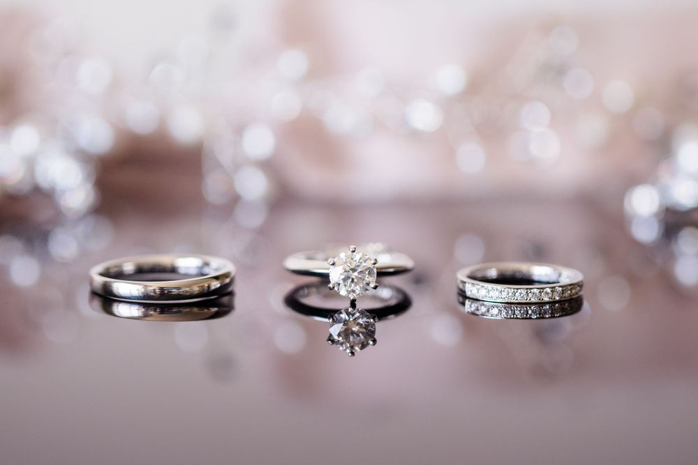 Three wedding rings with diamonds arranged artistically on reflective surface with bokeh background.