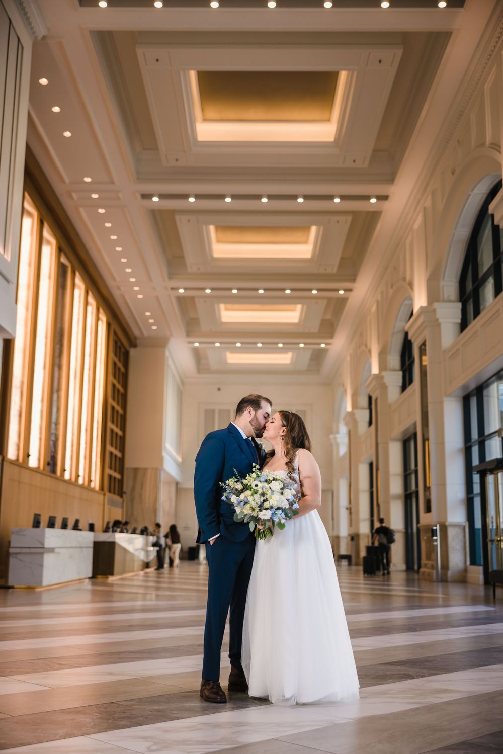 Wedding couple shares intimate moment in elegant hall with illuminated ceiling and polished floors.