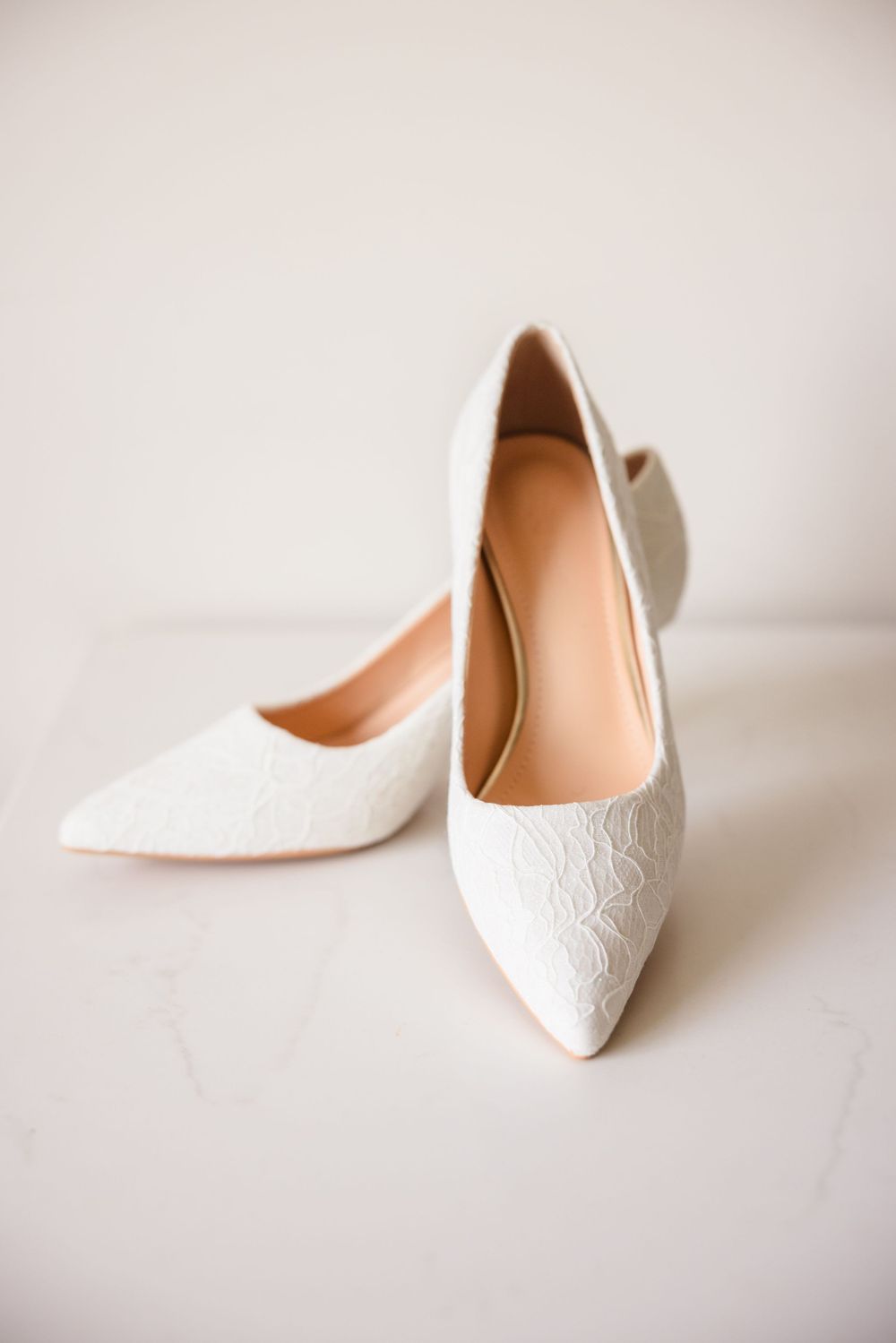 White lace pointed-toe wedding heels photographed against a light neutral background.