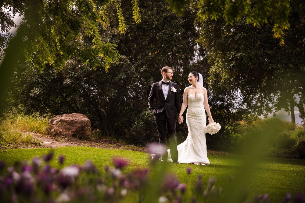 Wedding portrait in a garden with purple flowers and lush greenery.