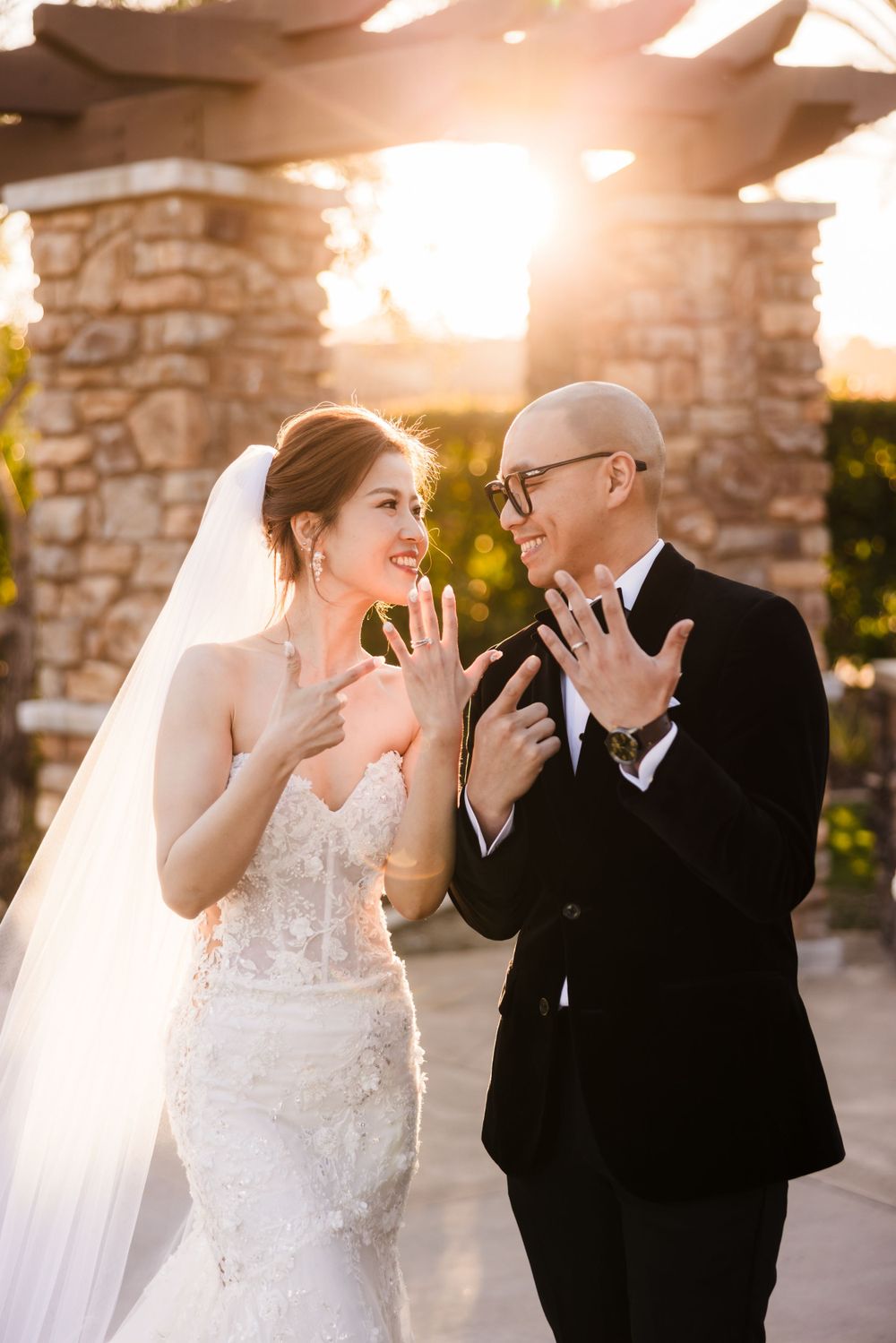 A joyful wedding moment captured in golden sunlight against stone pillars.
