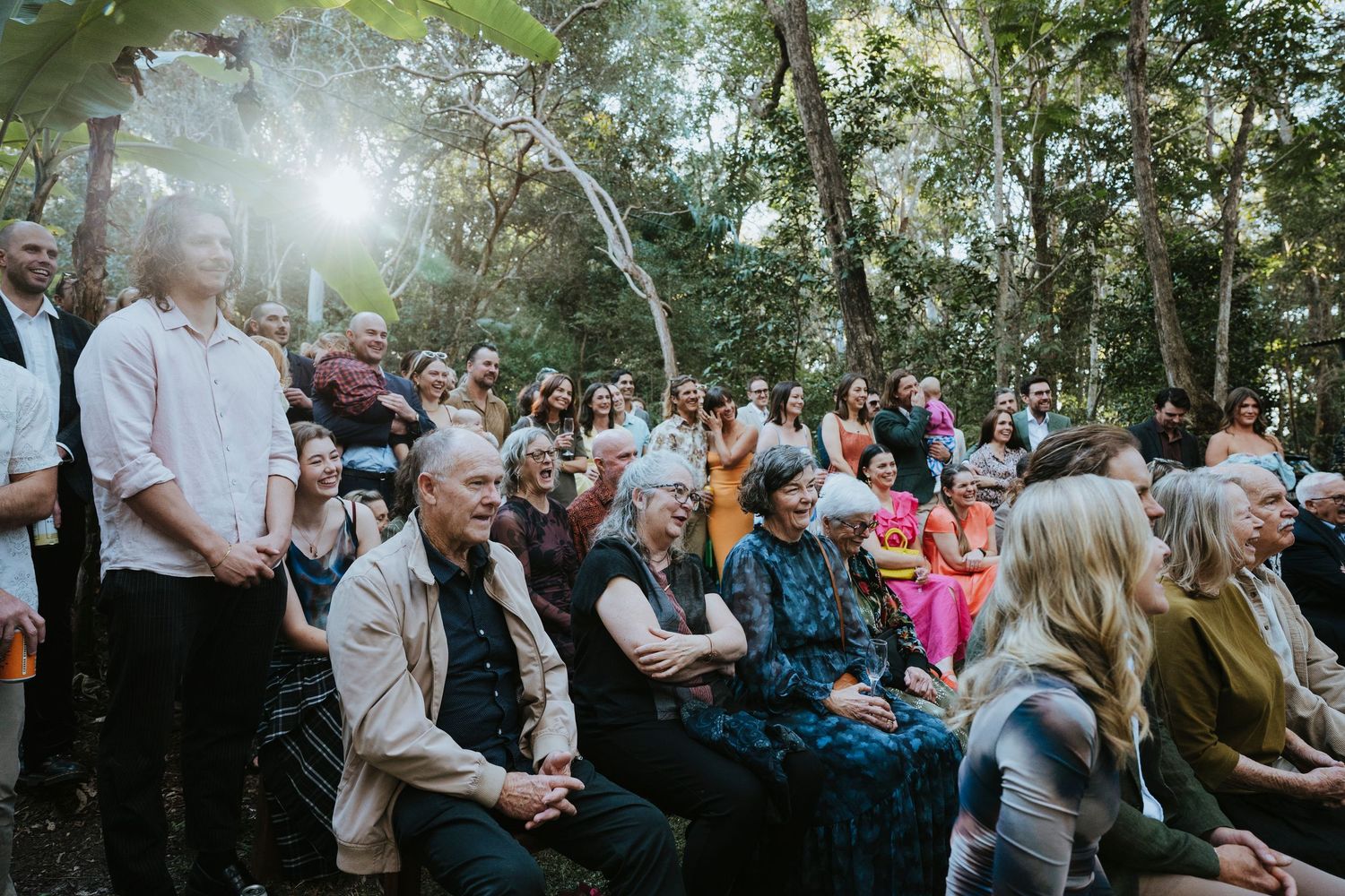 Wedding party guests dance and celebrate together with raised arms on a beach at sunset.