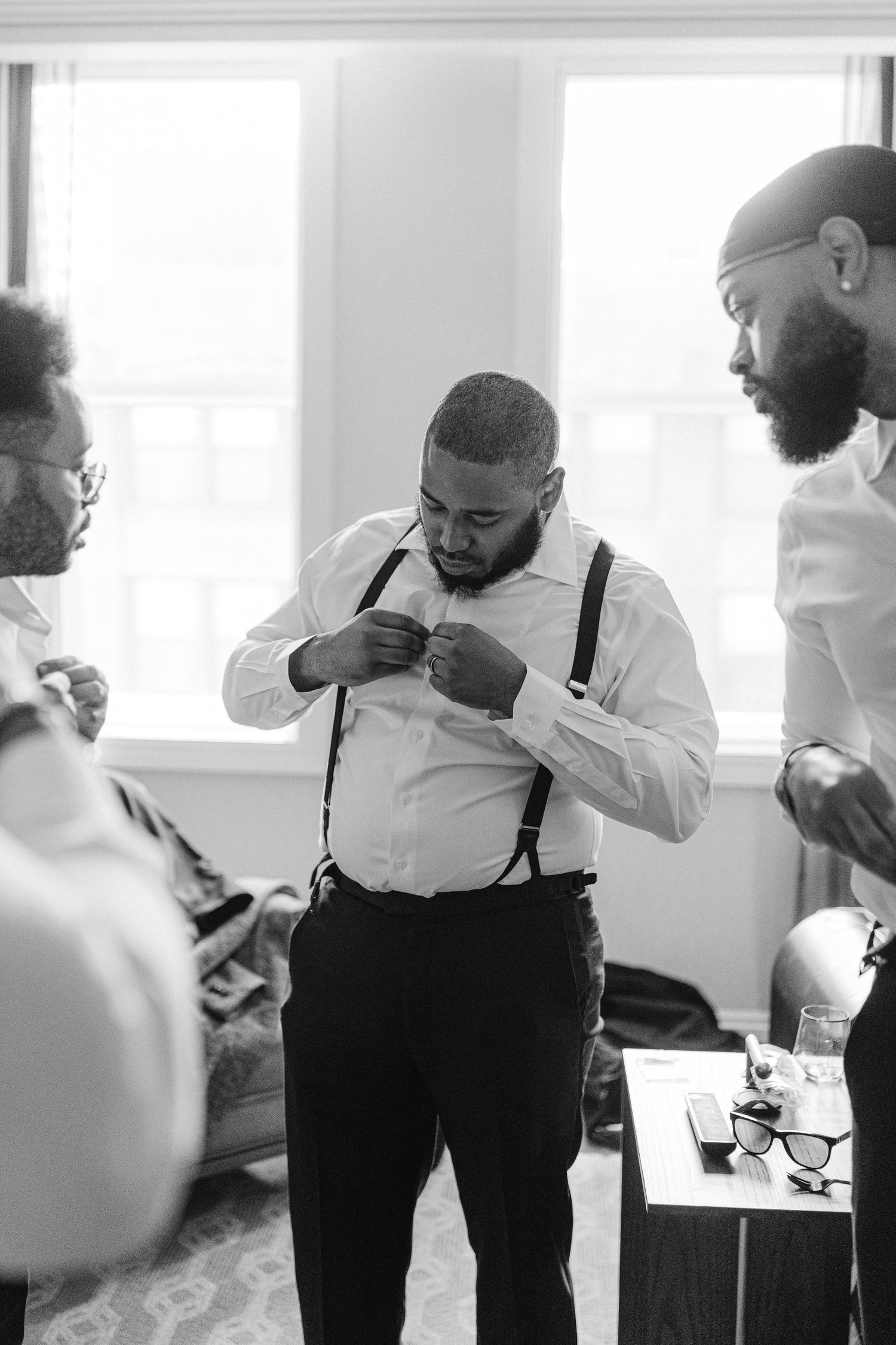 A person in white shirt and suspenders adjusts their outfit during formal preparation.