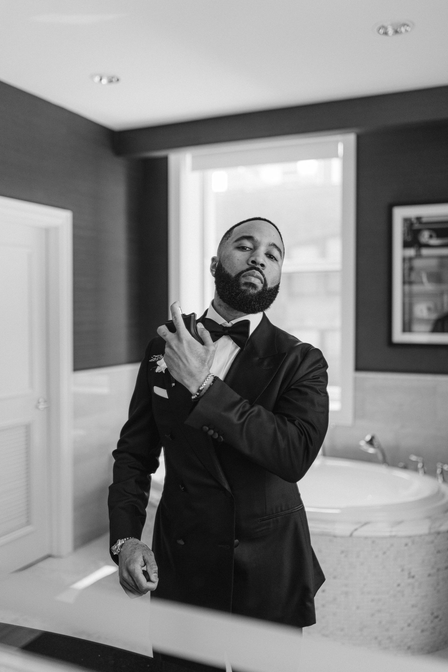 A reflection in a bathroom mirror shows a well-dressed figure adjusting a bowtie.