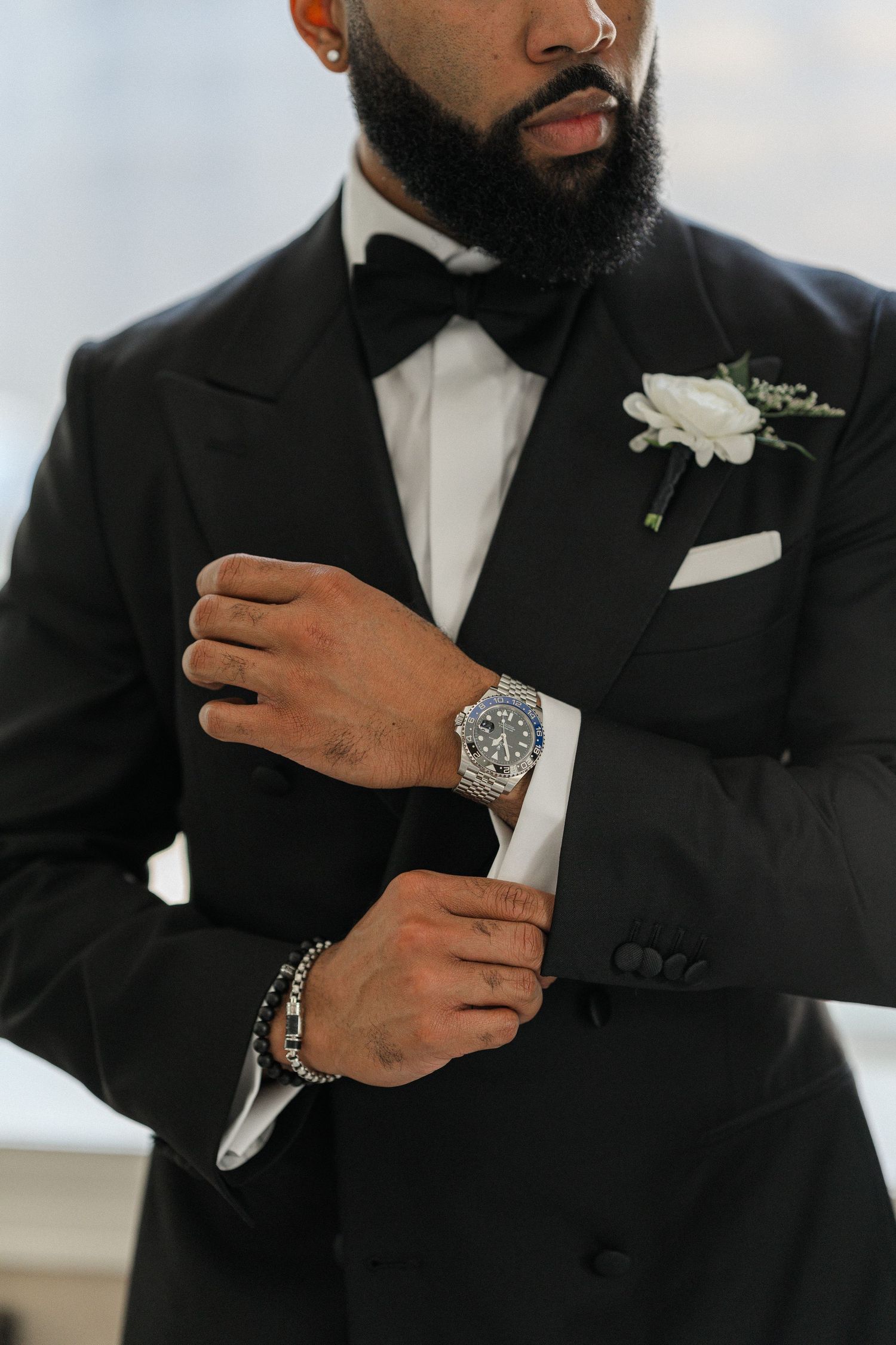 Close-up of a formal black tuxedo with bowtie, white boutonniere, and luxury watch.