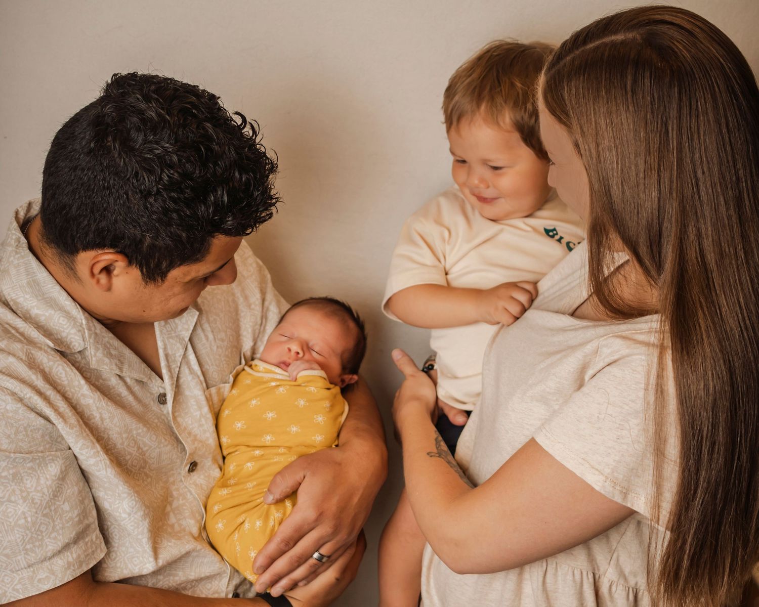 Father holds newborn girl while mother holds toddler brother, all are happy and engaged.
