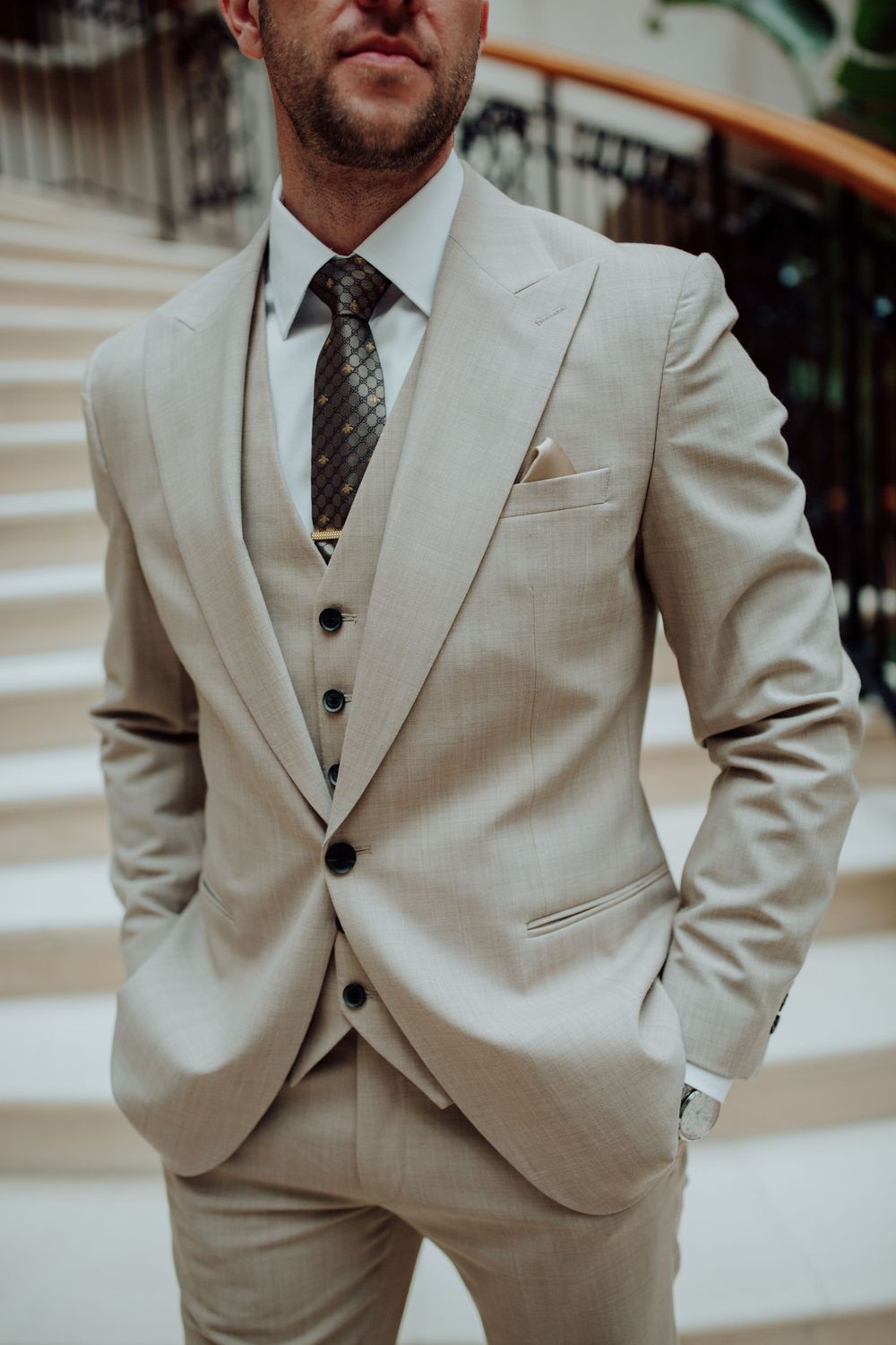 Close-up view of a beige three-piece suit with matching vest and patterned tie showcasing elegant formal menswear styling.
