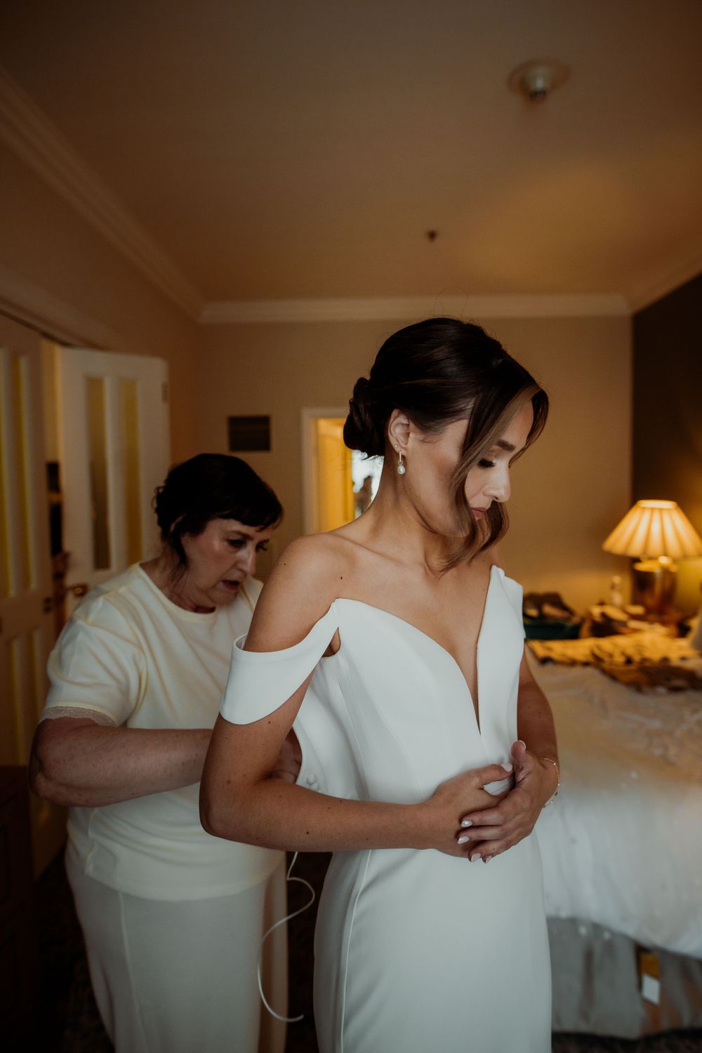 Wedding dress fitting scene with someone helping adjust the elegant white off-shoulder gown.  London wedding photographer. The landmark