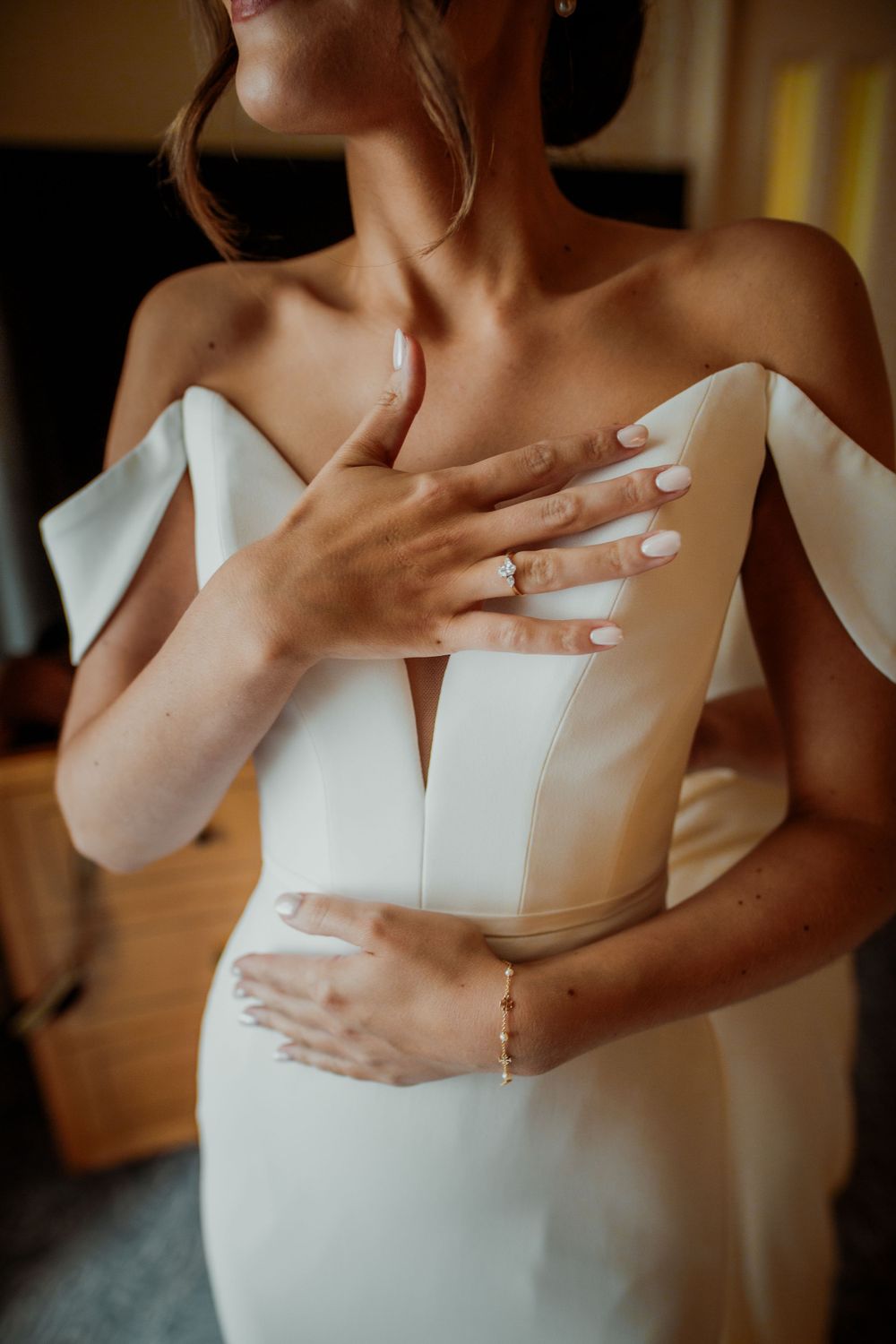 Detailed shot of white wedding dress bodice with off-shoulder design and delicate hand placement. London wedding photographer. The landmark