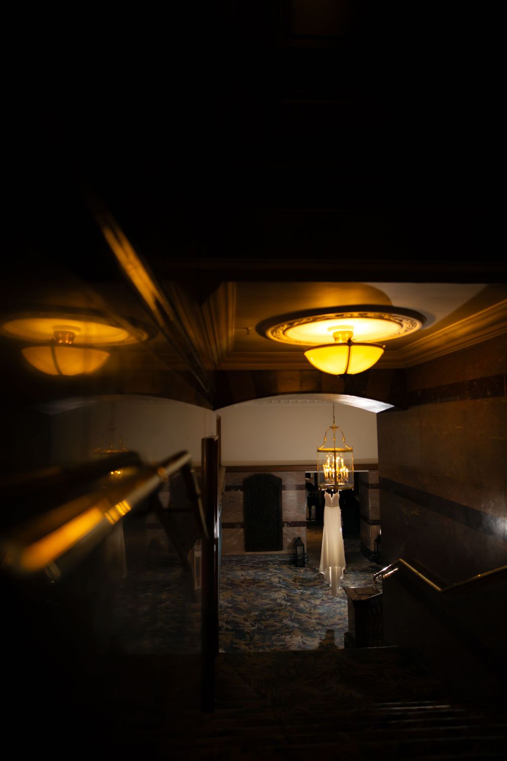 Moody hallway with warm lighting and a white dress hanging in the background.
